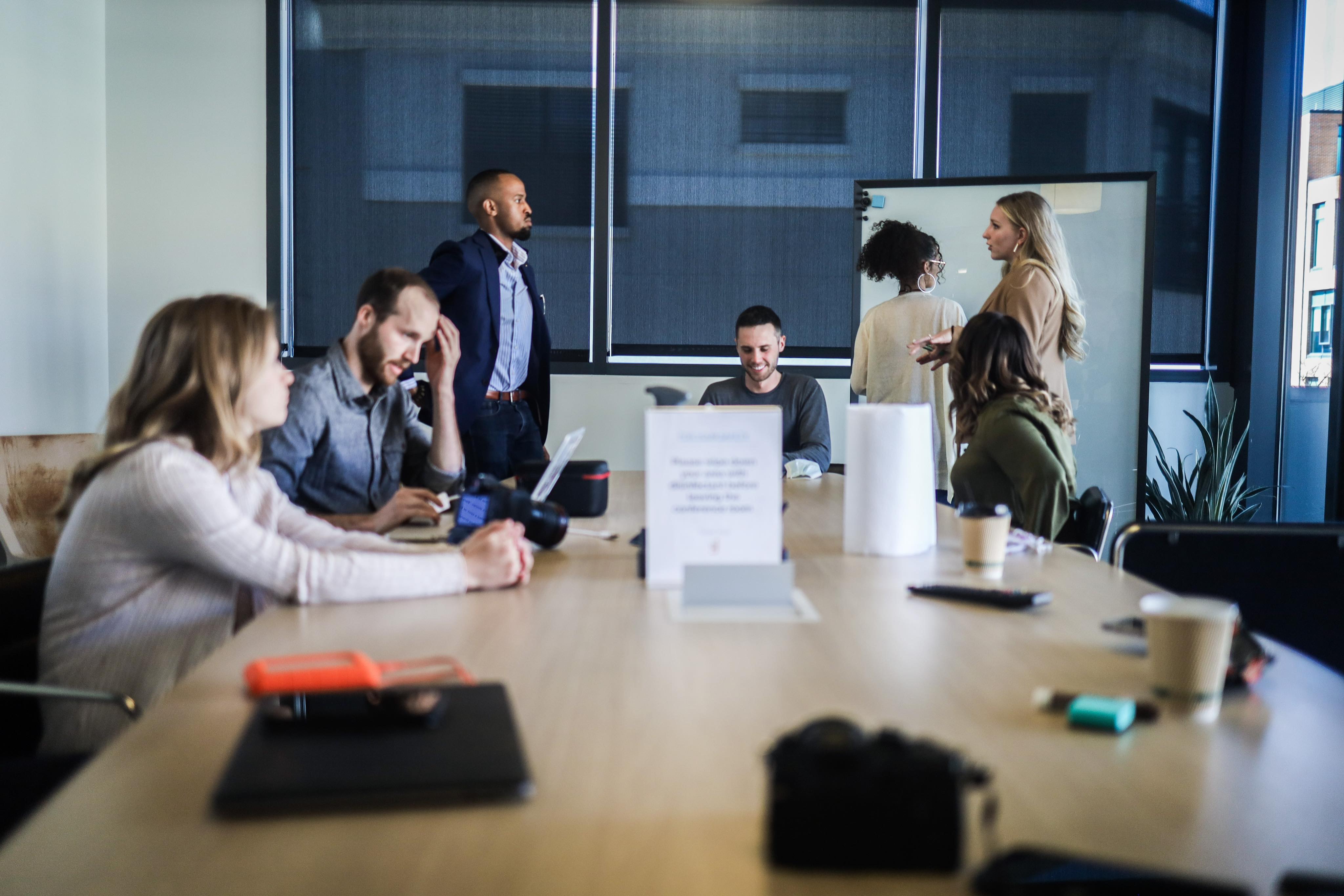 An illustration of a business team collaborating in a modern office to navigate state and federal RFPs. The scene includes individuals reviewing documents, analyzing charts, and using laptops, with a digital display featuring government seals, RFP forms, and contract terms. Growth symbols like arrows, maps of state and federal regions, and a handshake image highlight strategy and opportunity in government contracting.