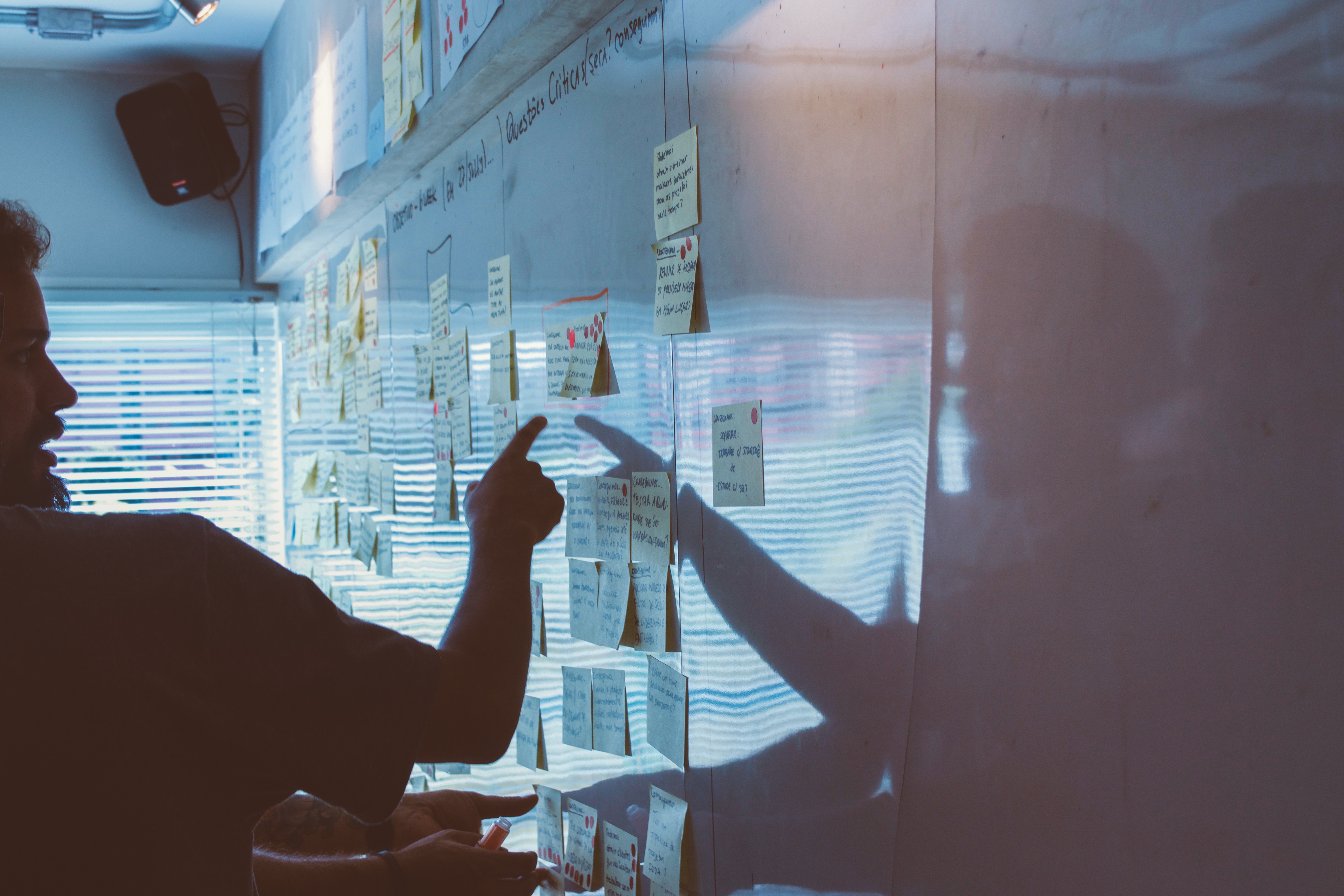 An illustration of a business team working collaboratively in a modern office, with additional team members joining virtually on large digital screens. Professionals are engaged in preparing proposal documents, analyzing charts, and planning strategies. Symbols of growth, such as upward arrows and interconnected nodes, emphasize teamwork, resource expansion, and success in proposal development.